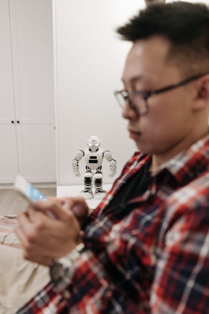 Man focused on smartphone with robot in background, depicting modern technology.